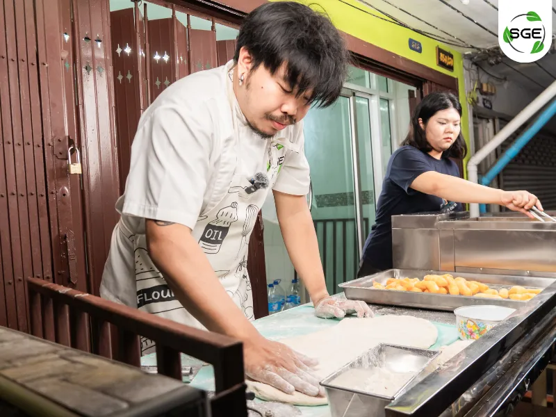 ผู้ชายกำลังปั้นแป้งปาท่องโก๋ ผู้หญิงกำลังทอดปาท่องโก๋ ในหม้อทอดน้ำน้ำมัน