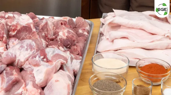 วัตถุดิบเปิดร้านไส้กรอกรมควัน มือผู้ชายกำลังจะเอาเนื้อหมูเข้าดครื่องหั่นหมู และมีเครื่องปรุงวางไว้บนโต๊ะ